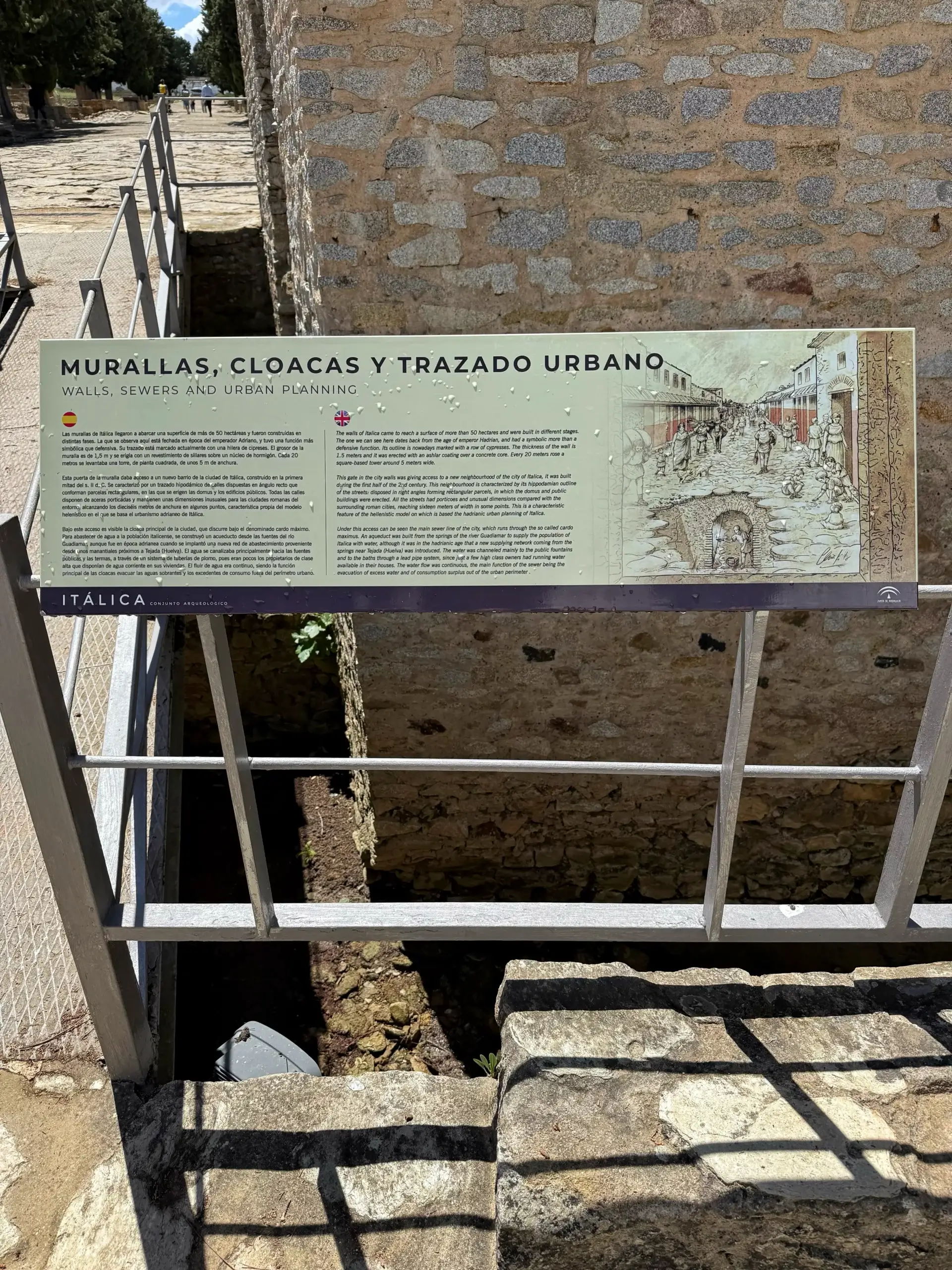 Stadtmauer, Kanalisation und Straßennetz Freigelegter römischer Abwasserkanal in Itálica mit Informationstafel zu Mauern, Kanalisation und Stadtplanung